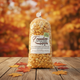 A clear plastic bag filled with golden yellow kettle corn on a round wooden coaster, set against a textured gray background. The bag features a white label for 'Freedom Kettle Corn of Arkansas' with 'First Cheddar' written on a small green badge.